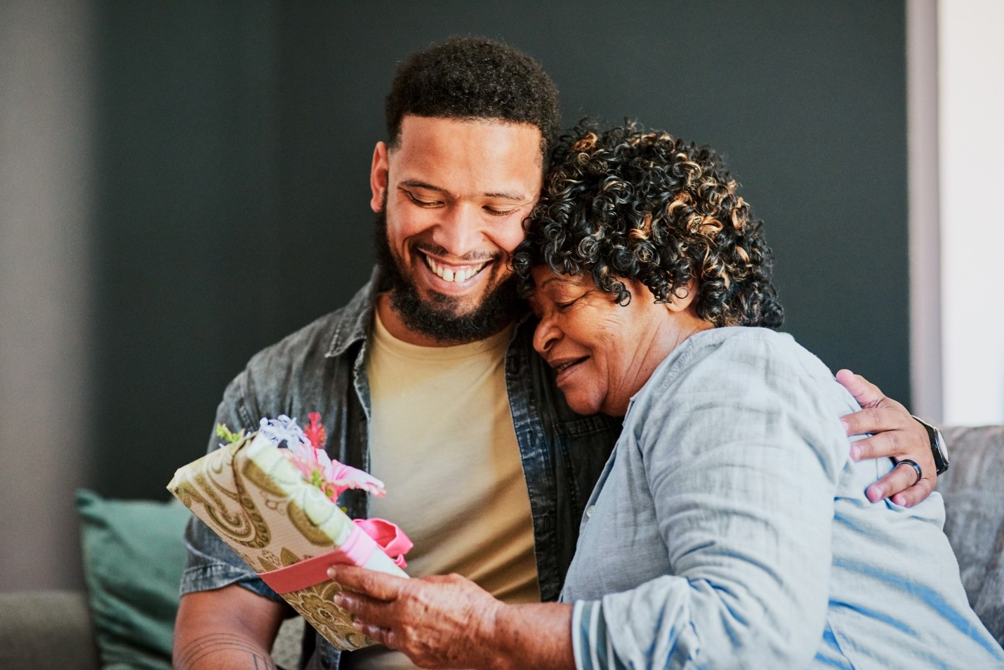 Man embraces his senior mother as he gives her a wrapped gift.