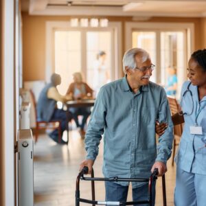 An older man walks with a caregiver at a senior living community.