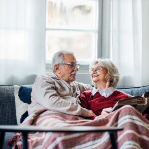 An older couple sits together on a couch smiling.