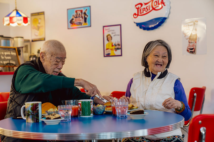 An elderly couple enjoying a meal together in a retro diner setting, with vibrant décor and cheerful expressions.