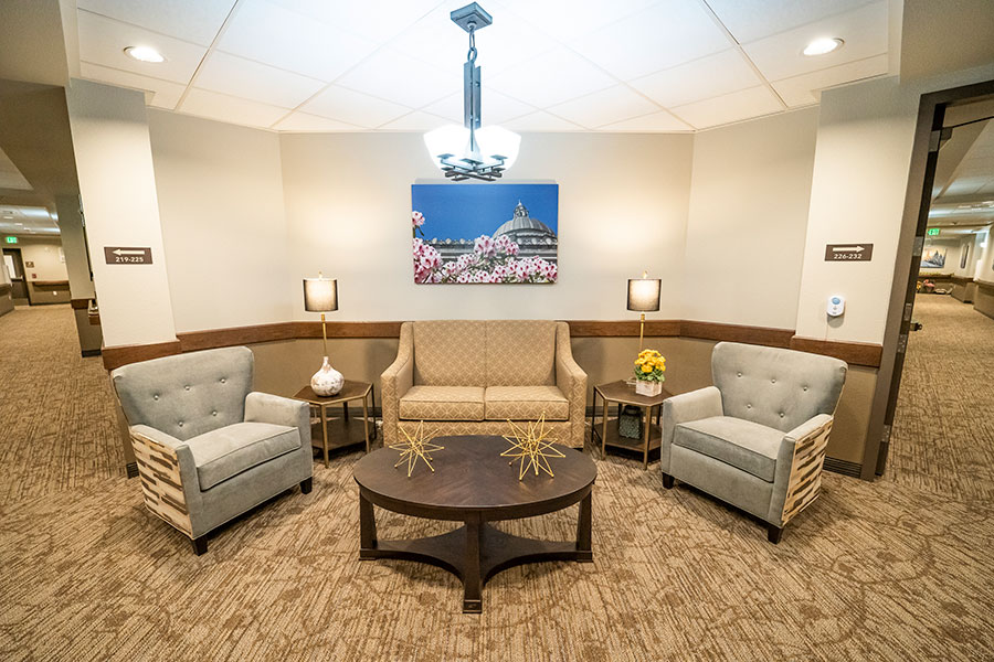 A cozy seating area with two armchairs, a sofa, a round coffee table, and decorative lighting, featuring a floral wall art piece.