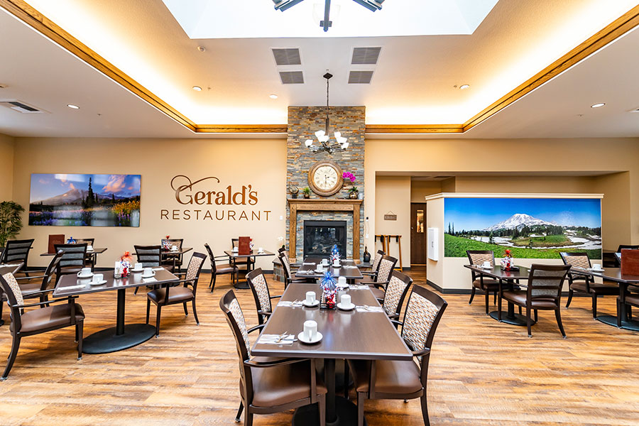 The image depicts the interior of Gerald's Restaurant, featuring wooden flooring, tables set with cups, a stone fireplace, and large scenic wall art. The space is well-lit and inviting.