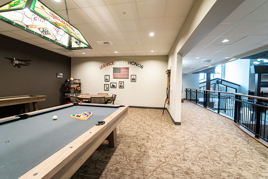 The image features a game room with a pool table, a decorative lamp, and a wall displaying the phrase 