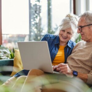 An older man and woman look at senior living communities on a laptop.