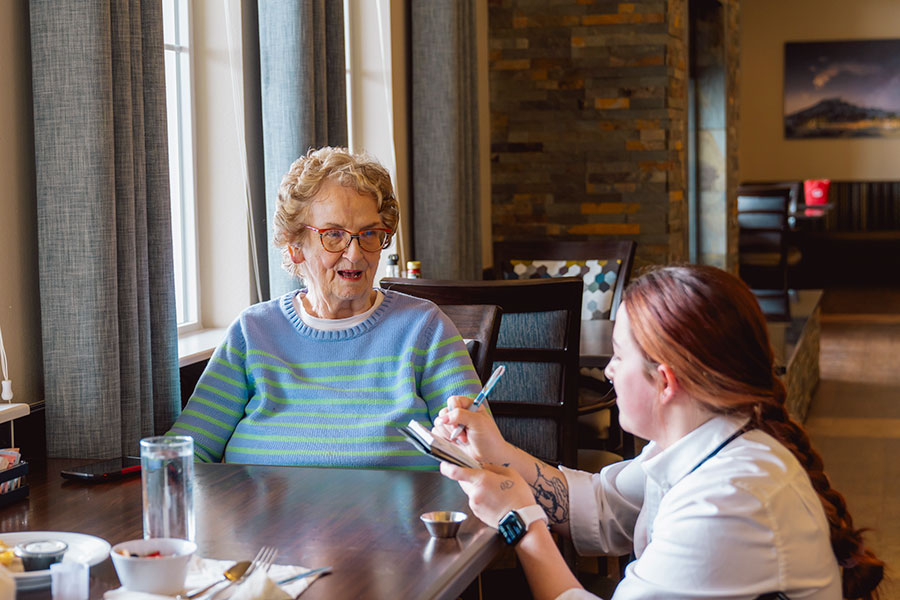 Elderly woman happily chatting with a caregiver in a restaurant.