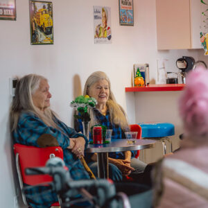 Two women chatting in a cozy, colorful cafe setting.