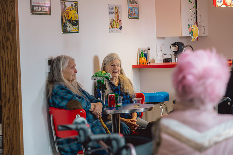 Two women chatting in a cozy, colorful cafe setting.