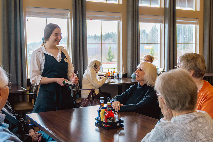 Waitress serving food in a dining area with seniors.