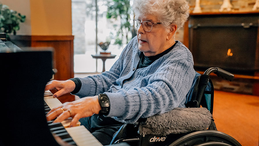 Elderly woman playing piano from a wheelchair indoors.