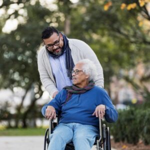 A family caregiver pushes his father in a wheelchair through a park